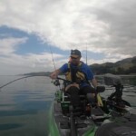 Angler fighting fish on softbait rod from kayak in calm coastal water