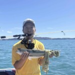 Angler holding a small kahawai on a boat with spinning rod across shoulders in New Zealand waters