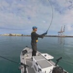 Angler fishing from small fishing boat with rod loaded in the cast