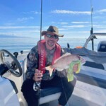 Angler holding snapper on small boat with fishing rod on calm open water